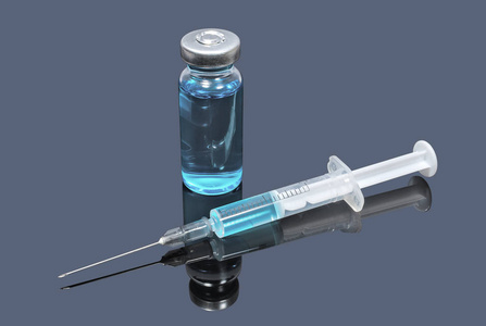 黑暗背景下的蓝色疫苗和注射器的医疗药瓶