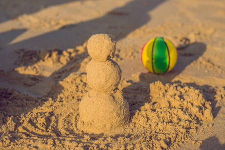 在红色的圣诞老人的帽子和太阳镜在阳光明媚的海滩沙质圣诞雪人。新的一年卡的度假概念