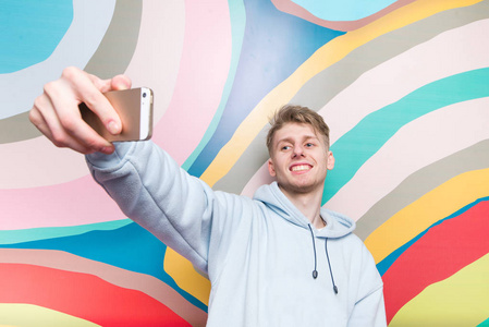 快乐的年轻人在彩色的抽象背景上做自拍。微笑的青少年在智能手机上拍照