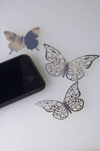智能手机依赖于白色的表面。在他周围的蝴蝶，饰品雕刻从箔