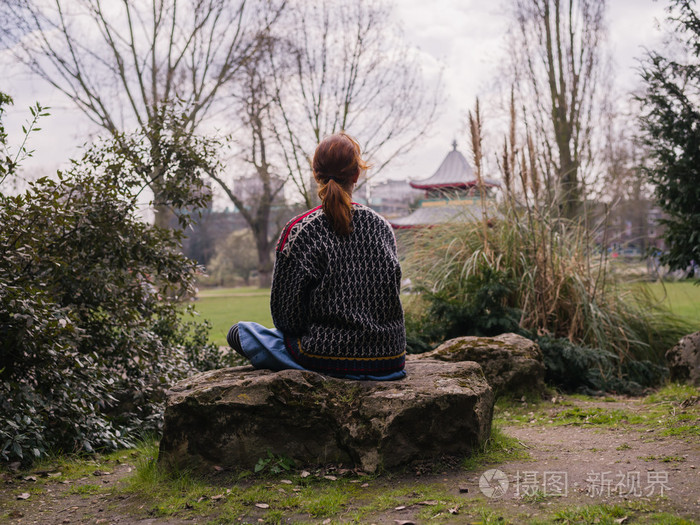 年轻的女人坐在公园的石头