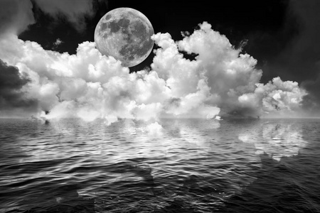 满月和云朵在暗黑的夜空中，反映在波浪海洋水