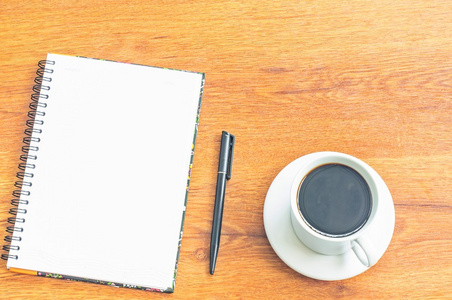 白色的咖啡杯，黑色的钢笔，笔记本上木背景