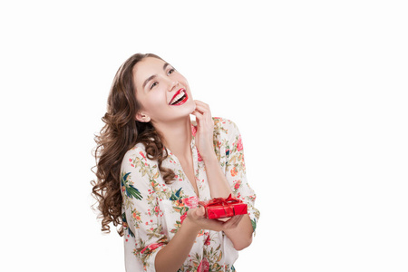 快乐的小女孩在她的手中享受礼物, 红色礼物盒。模型在白色背景下被隔离。美丽的卷曲的黑发与红色口红
