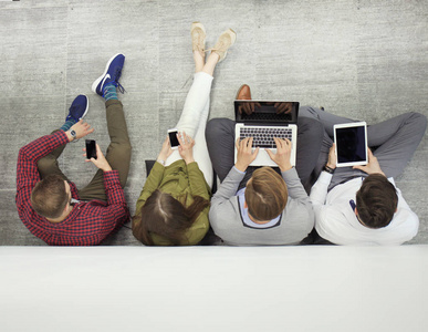 群吸引年轻人坐在地板上使用笔记本电脑，平板电脑，智能手机，微笑