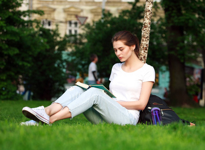 年轻的女学生在读一本书的城市公园