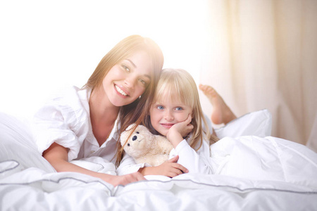 快乐充满爱的家庭。母亲和她的女儿儿童女孩躺在床上玩