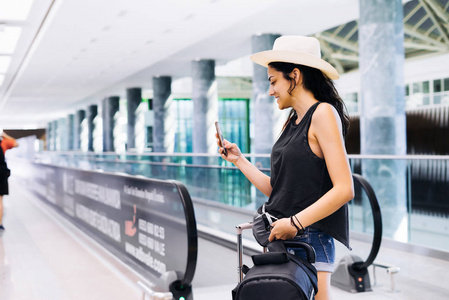 旅行在机场使用智能手机的女人。年轻的东部旅行者，检查与手机应用程序在终端或火车站的登机时间。旅游度假