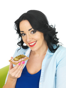 年轻女人吃一块饼干与德国香肠和小黄瓜