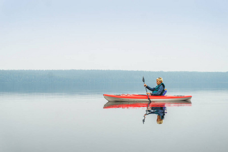 女人高兴地在平静的湖面上从红皮划艇桨