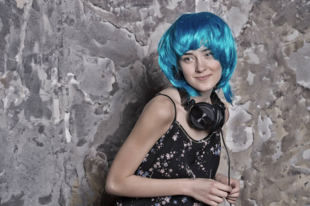 在蓝色假发戴着耳机在水泥墙上微笑着的女孩