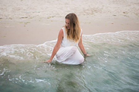 生活方式女人坐在一条白色的连衣裙，坐在海洋海岸水平图像