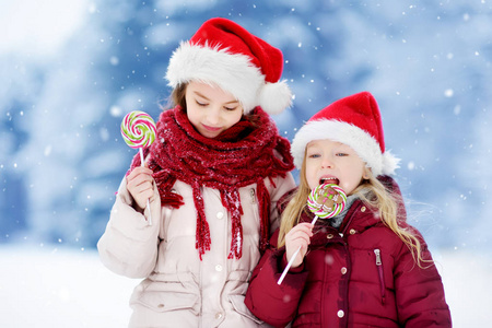 两个小姐妹在圣诞老人的帽子与棒棒糖