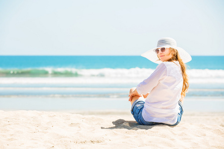 美丽的年轻女子坐在沙滩上，在阳光灿烂的日子享受暑假
