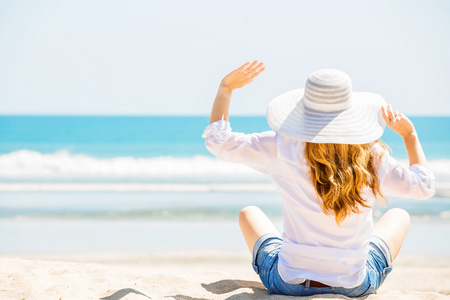 美丽的年轻女子坐在沙滩上，在阳光灿烂的日子享受暑假