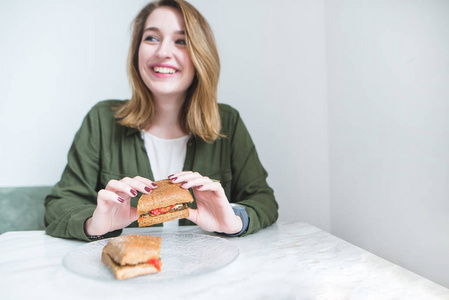 一个在餐桌上坐着微笑的女孩手中的开胃三明治。积极的女孩在餐桌上吃三明治。专注于三明治