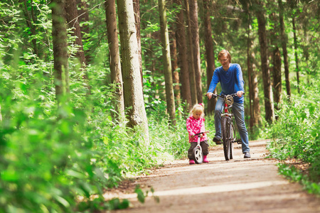 家庭体育父亲和女儿骑自行车在绿色森林