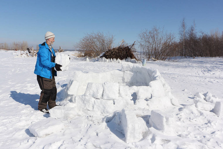 穿着蓝色夹克的男人在冬天的空地上建造一座冰屋