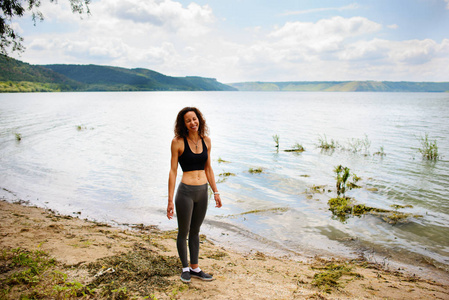 一个美丽的运动型女人站在运动服的湖岸上，准备行使