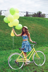 年轻的女人，穿着蓝色的衣服，用气球和复古自行车在公园里摆姿势