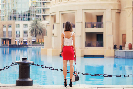 白衣瘦和高大的欧洲女人作物与小袋和高的高跟鞋，站在海滨在迪拜市中心附近顶尖和短的红裙子