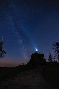 游客站在岩石上和指向夜空手电筒