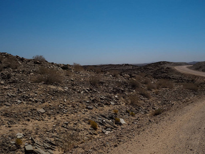 冒险旅程现场土路通过纳米布沙漠干旱景观趟山地平线与本地植物，劈石 清澈的蓝天
