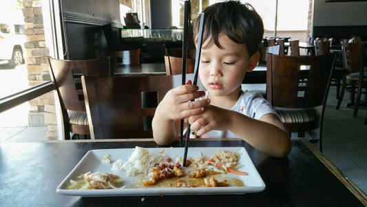 可爱的中国年轻人和白人男孩学习使用筷子餐厅