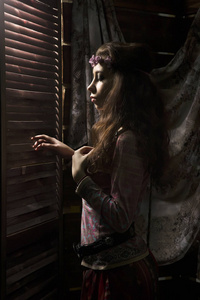 美丽的嬉皮波西米亚女人看着在黑暗的背景下关闭的窗口