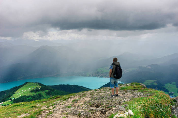 背包的男人站在山顶上的雨和远方期待的山脉和美丽的绿松石山 lake