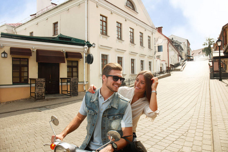 快乐的年轻夫妇骑滑板车在城里。英俊的男人和年轻的女人旅行。冒险和假期的概念