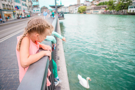 可爱的小女孩在户外在苏黎世，瑞士。孩子们在美丽的城市，靠近河流和天鹅