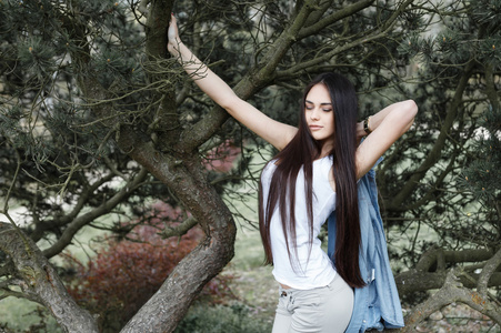 在杉树的背景下在公园里摆姿势的漂亮女孩