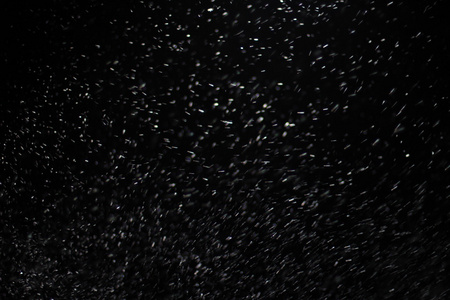 抽象的暴风雪纹理。在黑色背景上的散景灯拍摄的飞片雪花在空中