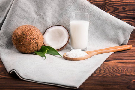 一篇作文的有机和明亮的棕色椰子，轻木勺子用磨碎坚果和天然椰奶暗棕色木制的桌子上。热带椰子