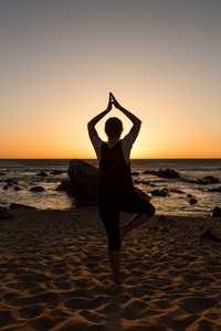 剪影年轻女子在日落时练瑜伽在海滩上