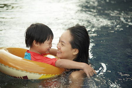 年轻的母亲和她的儿子开心一起玩在游泳池