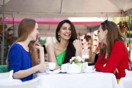 三个快乐女友女人坐在一张桌子在夏天 c