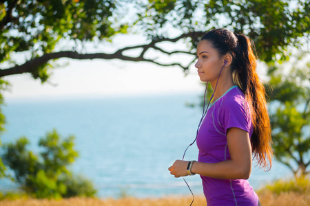 女性慢跑者在训练后的耳机听音乐。年轻运动的女人，在公园里行使附近的户外出海，喜欢带着耳机的音乐