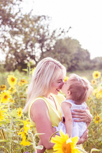 家庭沿着夏季开花字段。幸福的母亲和女儿在阳光下。夏天。向日葵