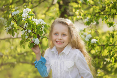 一个美丽的小女孩在春天开花花园的肖像。金发的盛开的花园里可爱的孩子