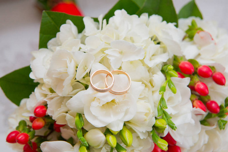 两个黄金结婚戒指躺上一束白色的花，结红色浆果