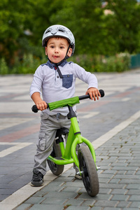 儿童男孩骑在他头戴头盔的第一辆自行车上的白色头盔。没有踏板的自行车