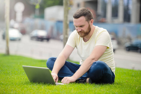 业务和自由。现代企业背后一台笔记本电脑在户外草地上胡子的男人