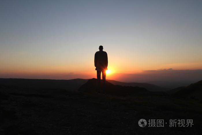 一个男人站在山上和迎接初升的太阳