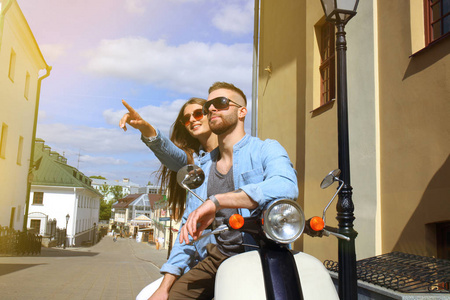 快乐的年轻夫妇骑滑板车在城里。英俊的男人和年轻的女人旅行。冒险和假期的概念