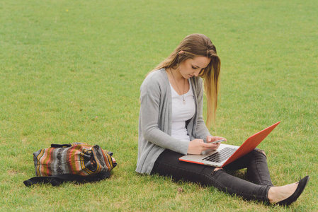 年轻的女孩坐在草地与智能手机和笔记本电脑上