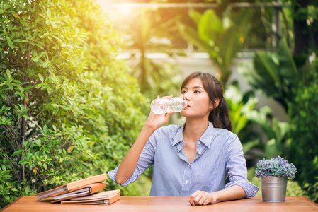 年轻漂亮的黑发女人在夏天绿色公园穿蓝色 t 恤饮用水的肖像