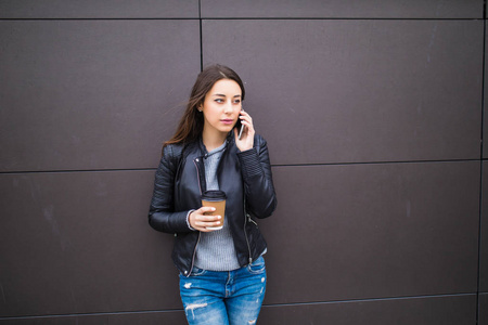 快乐的年轻女人发短信和在城市外面举行咖啡而靠在墙上