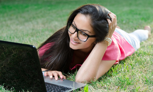 一台笔记本电脑，躺在草地上的漂亮女孩